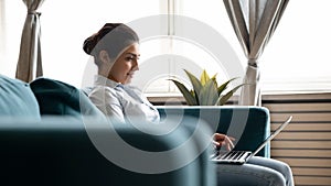 Indian female sit on couch working on laptop from home