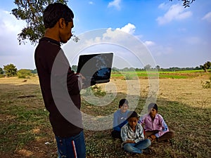 indian poor villager giving training about laptop computer system at green field in india January 2020