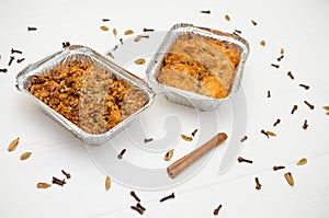 Indian food, fruit pies, subhadra and mithai, in foil plates on white background, with seeds, spices, cinnamon