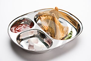 Indian food snack Samosa served in a stainless steel plate with tomato ketchup