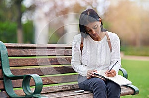 Indian girl, student and writing notes at park for education, learning or studying at university on bench in garden