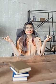 Indian girl wearing casual clothes sitting on the table relaxed and with eyes closed during meditation gesture with