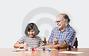 Indian grandfather helping grand daughter drawing & painting with colours and brush on paper at home