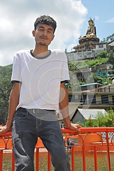 A Indian guy sitting on safety barrier by lake and beautiful hilly area of Tso-Pema and statue of Padmasambhava Guru Rinpoche