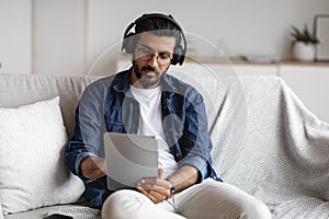 Indian guy spending time at home with digital tablet and wireless headphones