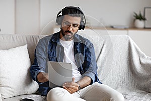 Indian guy spending time at home with digital tablet and wireless headphones photo