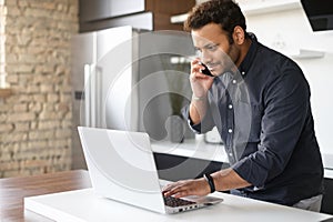 Indian guy is talking on the smartphone and using laptop at home