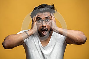 Indian handsome guy expressing shock and despair, touching his head with hands.