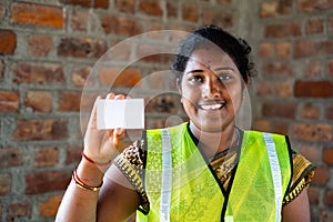 Indian happy smiling labour women showing empty card by lookig at camera - concept of empoyee id card, advertisement and