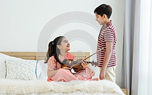 Indian happy teenage boy, girl sibling teaching, learning, playing, practicing violin musical instrument together at cozy home in