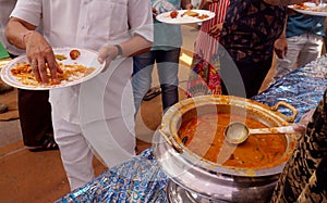 Indian Hindu volunteer serve the vegetable curry to the devotee, in free distribution of prasad or food or meal in a temple