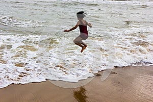 Indian kid girl jumping against approaching wave on puri sandy beach in seashore expressing joy and excitement