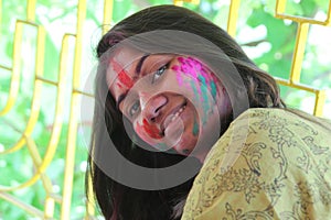 An Indian lady in 30s with face full of vibrant colours and looking towards the camera and smiling