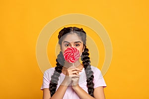 Indian lady holding lollipop, covering mouth with candy