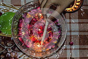 A indian lady lit up a jar is which is loaded with rose and candle on indian festival diwali deepawali with fire  on table