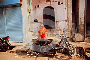 Indian lady sitting on motorbike on poor people area of old city