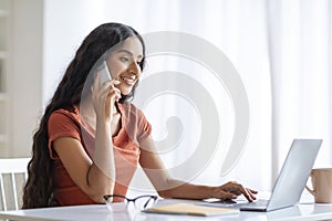 Indian lady using laptop, speaking on smartphone at home office