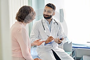 Indian male doctor physician consulting senior patient filling medical form.