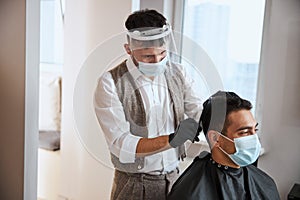 Indian male in protective mask spending time in beauty salon making the hair cut
