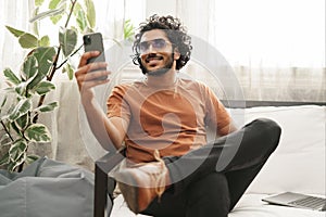 Indian male using his phone, laptop at arm& x27;s reach, in a warm room setting