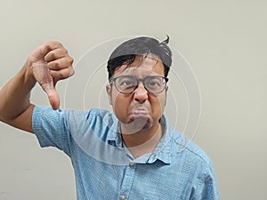 Indian male wearing glasses and a blue shirt expressing his dissatisfaction by making a thumb down