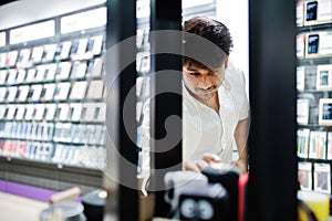 Indian man customer buyer at mobile phone store chooses the goods on the shelf. South asian peoples and technologies concept.