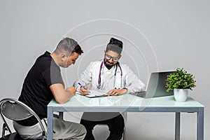 Indian man doctor prescribes prescription for pacient sitting at the desk medical office, isolated on white background