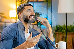 Indian man freelancer working talking with client on retro old-fashioned wired telephone at home