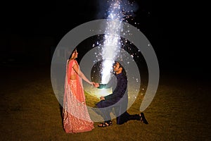Indian man on his knees holding her her girlfriends hand proposal in traditional wear celebrant diwali festival with firecrackers