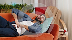 Indian man lying on sofa feeling sudden strong abdominal stomach ache gastritis poisoning diarrhea