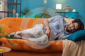 Indian man lying on sofa feeling sudden strong abdominal stomach ache, gastritis problem, diarrhea