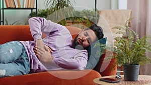 Indian man lying on sofa feeling sudden strong abdominal stomach ache, gastritis problem, diarrhea