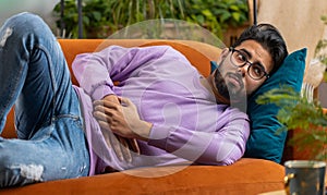 Indian man lying on sofa feeling sudden strong abdominal stomach ache, gastritis problem, diarrhea