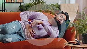 Indian man lying on sofa feeling sudden strong abdominal stomach ache, gastritis problem, diarrhea