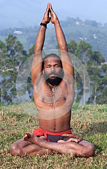 Indian man meditating in lotus yoga pose on green grass in Kerala, India