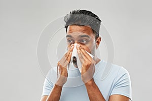 Indian man with paper napkin blowing nose