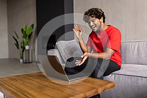 Indian man relaxing on couch while video calling using laptop at home. Asian man sitting on sofa and making a video call. Smiling