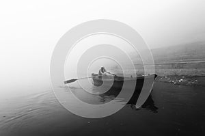 Indian man sailing on the boat on sacred river Ganges at cold foggy winter morning