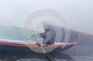 Indian man sailing on the boat on sacred river Ganges at cold foggy winter morning