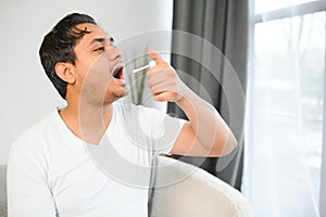 Indian man sick at home, cold, flu. A man uses a throat spray