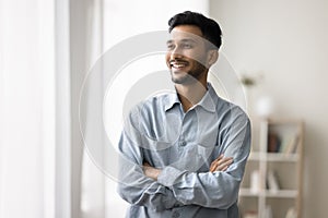 Indian man standing with arms crossed smiling looking away