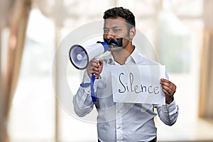 Indian man with taped mouth holding poster with inscription Silence.