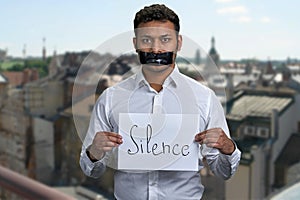 Indian man with taped mouth holding poster with inscription Silence.