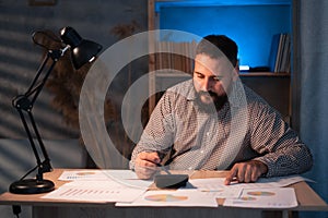 Indian man using a calculator to calculate finances at home at night. businessman taxation, accounting, statistics