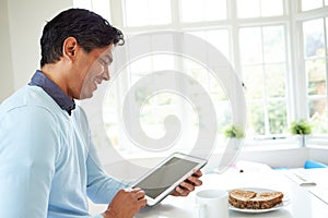 Indian Man Using Digital Tablet Whilst Eating Breakfast