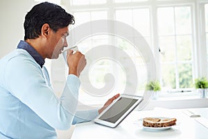 Indian Man Using Digital Tablet Whilst Eating Breakfast