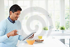 Indian Man Using Digital Tablet Whilst Eating Breakfast