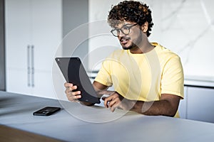 Indian man using digital tablet white sitting in the kitchen