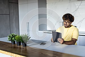 Indian man using digital tablet white sitting in the kitchen