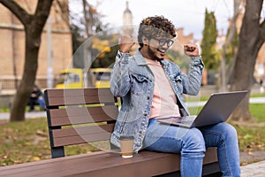 Indian Man using laptop sitting on yard of business center and happy because he win on the bets